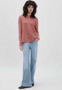 Hellrosa Langarmshirt kombiniert mit hellblauen Schlagjeans. Die Jeans haben eine verblichene Textur und ein klassisches Fünf-Taschen-Design.