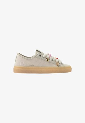 Sneaker beige chiaro modello basso con suola in gomma e lacci bianchi soffici adornati con piccoli accessori colorati a forma di ciondolo.