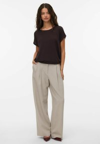 Haut marron foncé à manches courtes associé à un pantalon large beige clair. Le pantalon est doté de plis sur le devant et est porté avec des chaussures à pointes.