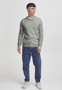 Pull en tricot gris avec un col rond, associé à un jean en denim bleu et des baskets blanches. Texture lisse et coupe décontractée.