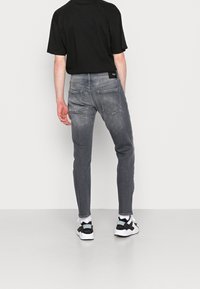 Šedé džíny z denimu s úzkým střihem, vybavené zadními kapsami a látkovou visačkou na pásku, spárované s černým tričkem s krátkým rukávem.