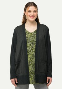 Mörkgrå cardigan med avslappnad passform, ribbad textur, öppen front och två framfickor, lagd över en blommig grön klänning.