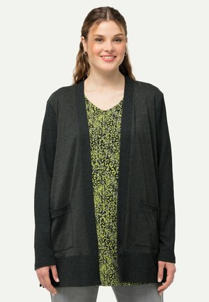 Cardigan gris foncé avec une coupe décontractée, texture côtelée, ouverture devant et deux poches avant, superposé sur une robe verte à fleurs.