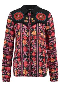 Chemise noire à manches longues avec une broderie florale rouge, rose et jaune vibrante et deux grands motifs floraux circulaires sur le plastron de la poitrine.