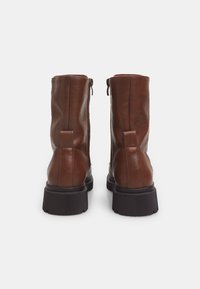 Botas de tobillo de cuero marrón con una textura suave, cremallera lateral y una suela de goma negra resistente. Cuentan con un pequeño tacón y una lengüeta en la parte posterior para facilitar su puesta.