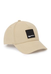 Gorra de béisbol beige hecha de tela texturizada con un parche cuadrado negro que presenta texto blanco en la parte frontal. Visera curvada y parte trasera ajustable.