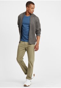 Grå ribbe cardigan over en blå t-skjorte, beige bukser og hvite sneakers med brune detaljer. Uformelt antrekk med en avslappet passform.