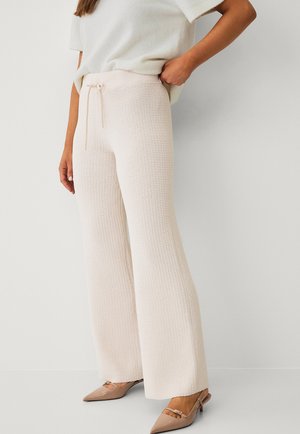 Lichtroze, gebreide wijde broek met een drawstring taille, gecombineerd met beige instappers met een kleine accentgesp. Glad textuur.