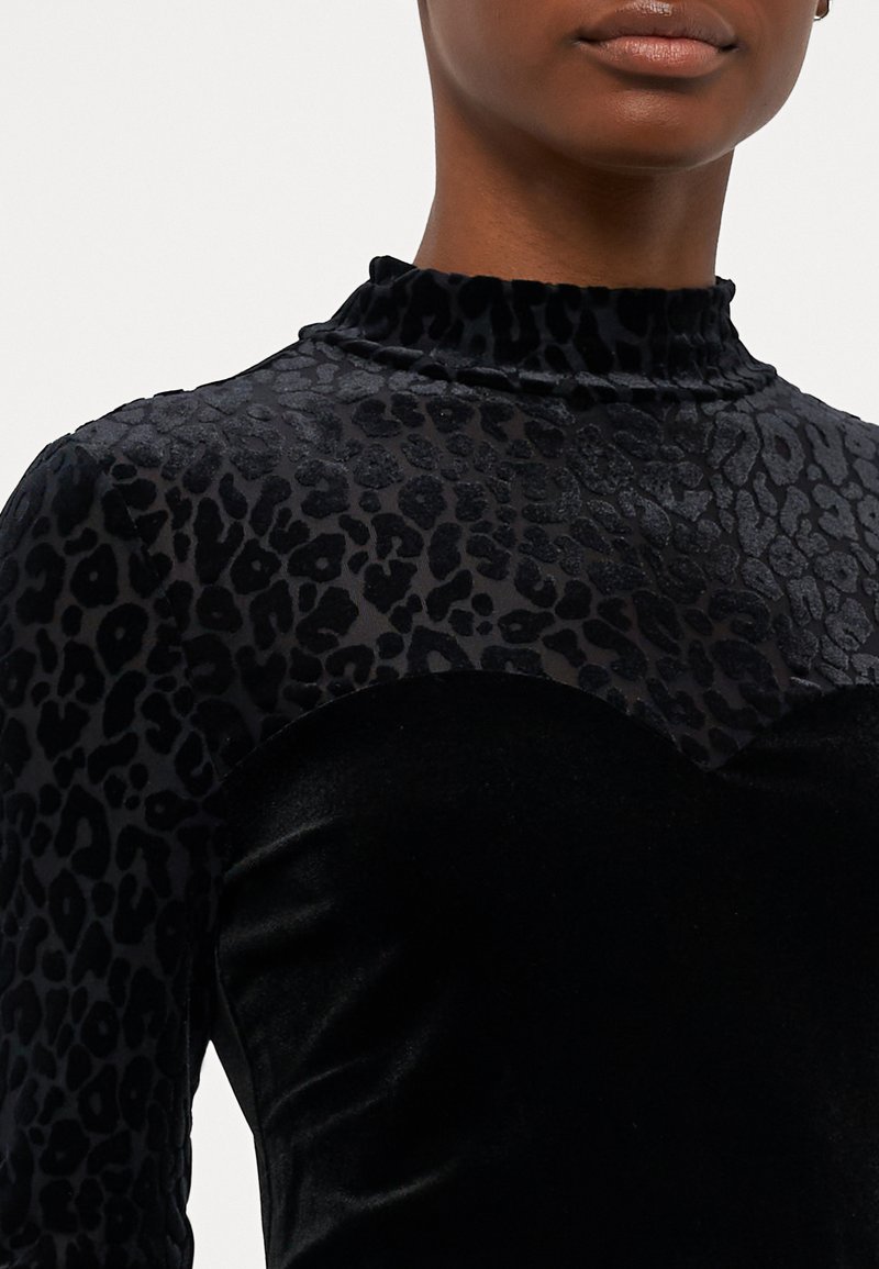 Abito nero con corpino in velluto e parte superiore trasparente con stampa leopardata. Il colletto alto e le maniche lunghe aggiungono dettagli al design.