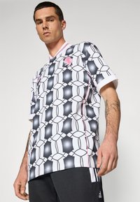 Camisa de manga corta con un patrón geométrico en blanco y negro, acentos en rosa y un diseño de escote en V. Fabricada con un material ligero y una textura suave.