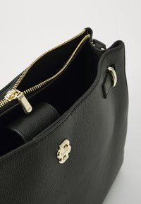 Black leather handbag with a textured finish, gold zipper, and metal hardware. The interior is partially visible, showcasing its spacious design.