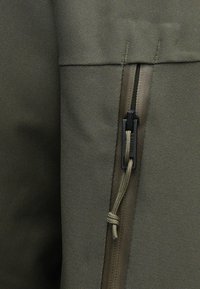 Maslina zelena tkanina s teksturiranim završetkom, s bočnim patentnim zatvaračem s crnim kvačilom i užetom za podešavanje.