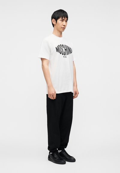 Άσπρο βαμβακερό μπλουζάκι με μαύρο λογότυπο "MOSCHINO", συνδυασμένο με άνετο μαύρο παντελόνι και μαύρα αθλητικά παπούτσια. Απλός σχεδιασμός και μινιμαλιστικό στυλ.