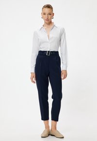 Vit skjorta med lång ärm, kombinerad med högmidjade marinblå byxor med ett bälte och silverfärgad spänne. Beiga loafers fulländar looken.