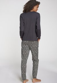Schwarzes Langarmshirt, kombiniert mit gemusterten Hosen, die ein diamantförmiges Design in Schwarz und Weiß aufweisen. Der Stoff wirkt weich und leicht.