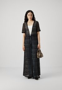 Svart blonde lang kimono med korte ermer, med et geometrisk mønster og løs passform, lagd over en hvit topp og paret med en liten beige veske.
