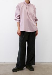 Camicia lunga color lilla con bottoni, abbinata a pantaloni in velluto a coste scuri a gamba larga e scarpe platform nere chunky.