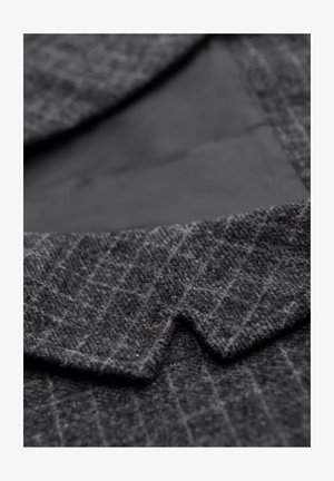 Tissu en laine grise avec un motif en chevrons, dotée d'un col aiguisé et d'une doublure noire lisse en dessous. Texture douce et forme structurée.