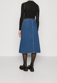 Mörkblå denim midi-klänning med rak skärning, detalj på baksaumen och nederkant som slutar under knäet. Bärs med svarta skor och strumpbyxor.