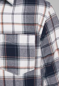 Gevlekt flanellen shirt met marineblauwe, witte en oranje strepen; bevat een borstzak; gestructureerde stof met een klassiek ruitpatroon.