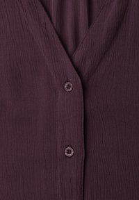Gros plan sur un tissu texturé violet foncé avec un col en V et deux boutons assortis étiquetés "Street One Studio."
