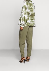 Grøn og hvid tie-dye bluse med puffede ærmer, parret med olivengrønne bukser. Sorte højhælede sandaler fuldender outfittet.