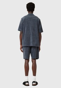 Donkergrijs T-shirt met korte mouwen en bijpassende shorts, gemaakt van een gestructureerde stof. Inclusief zwarte sandalen en witte sokken voor een casual look.