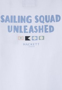 Tessuto bianco con grande testo blu "SAILING SQUAD UNLEASHED," con forme geometriche colorate e "HACKETT LONDON" in testo più piccolo sotto.