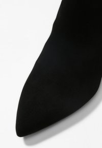 Svart mocka stilettklack med spetsig tå. Slät yta, minimalistisch design och strömlinjeformad silhuett som framhäver eleganta konturer.