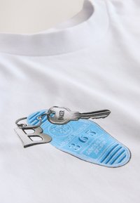 Balta medžiaga su atspausdintu mėlyno motelio raktų žymeklio dizainu, sidabriniu raktu su užrašu „BAKER“ ir stilizuotu „B“ raktų pakabuku.