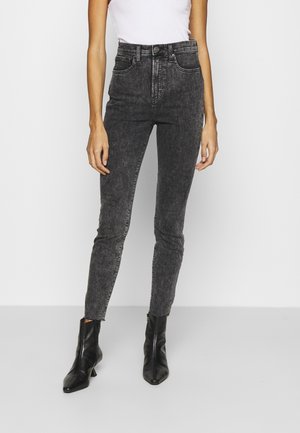 Hochtaillierte schwarze Jeans mit einem ausgewaschenen Stoff, ausgestattet mit Fronttaschen und einem Knopfverschluss, kombiniert mit spitzen schwarzen Ankle Boots.