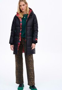 Čierny puffový kabát s kvetinovou podšívkou, v kombinácii s nohavicami s leopardím vzorom a zelenými topánkami. Dlhé rukávy s priliehavými manžetami.