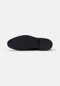 Suola nera della scarpa con texture liscia, punta rotonda e motivo di battistrada minimale. Presenta un leggero tacco e due dettagli dorati vicino al tacco.