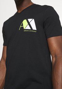 Svart bomull t-shirt med v-ringning och tryckt logotyp i vitt och neongrönt på vänster bröst. Korta ärmar.