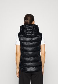 Czarna pikowana kamizelka z kapturem, o połyskującej teksturze i dopasowanym kroju. Widok z tyłu nie pokazuje żadnych zewnętrznych kieszeni.