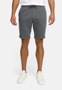 Shorts en tricot gris avec un waistband à cordon de serrage, des poignets roulés et des poches latérales ; associés à des baskets blanches. Design simple et tissu texturé.