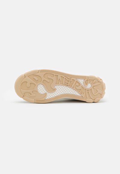 Semelle d'une sneaker en caoutchouc beige doux avec des motifs de grip texturés et une section en maille blanche, présentant des lettres en relief.
