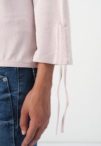 Stripet langermet topp i lys rosa og hvit, med mansjetterte ermer med sløyfer, kombinert med blå denimjeans.