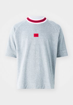 Helles graues T-Shirt mit kurzen Ärmeln und geripptem Kragen, der rot-weiße Streifen aufweist. Zentrales rotes quadratisches Patch mit "HUGO"-Logo. Weiche Stofftextur.