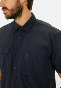 Kurzarmpoloshirt in Marineblau aus leichtem Material, mit Button-Down-Kragen, zwei Brusttaschen und einem Reißverschlusstaschedetail.
