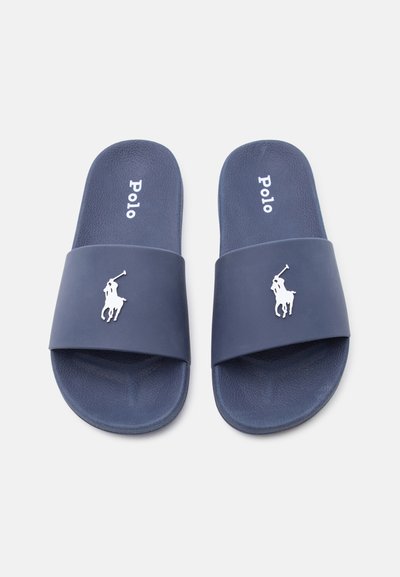 Ζευγάρι από slides Polo μπλε ναυτικού χρώματος με λευκό λογότυπο παίκτη πόλο στα λουράκια, φωτογραφημένα σε ανοιχτό φόντο.