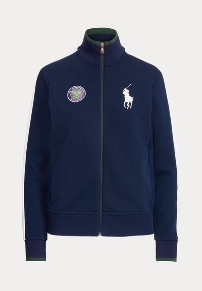 Marinblå zip-up-jacka med hög krage, vitt broderat hästlogo, lila Wimbledon-märke och kontrasterande vita sidostripes. Mjuk tygstruktur.