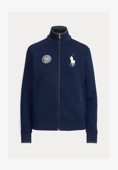Marinblå zip-up-jacka med hög krage, vitt broderat hästlogo, lila Wimbledon-märke och kontrasterande vita sidostripes. Mjuk tygstruktur.