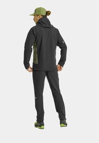 Black softshell jacket with green accents, fitted design. Paired with black pants and black shoes featuring green soles. Mesh cap.
