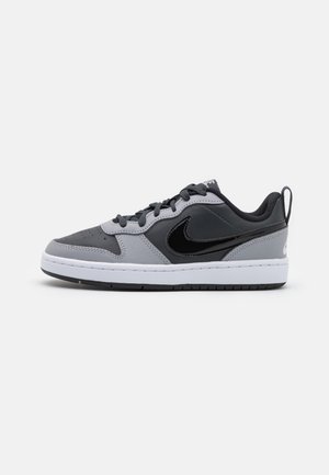 Low-top sneaker i grå og sort med sort swoosh-logo, hvid sål, snørelukning og trækflap ved hælen på ensfarvet baggrund.