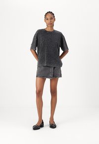 Svart denim kortärmad skjorta med pärldekorationer, tillsammans med en matchande grå denimkjol. Eleganta svarta skor fulländar outfiten.