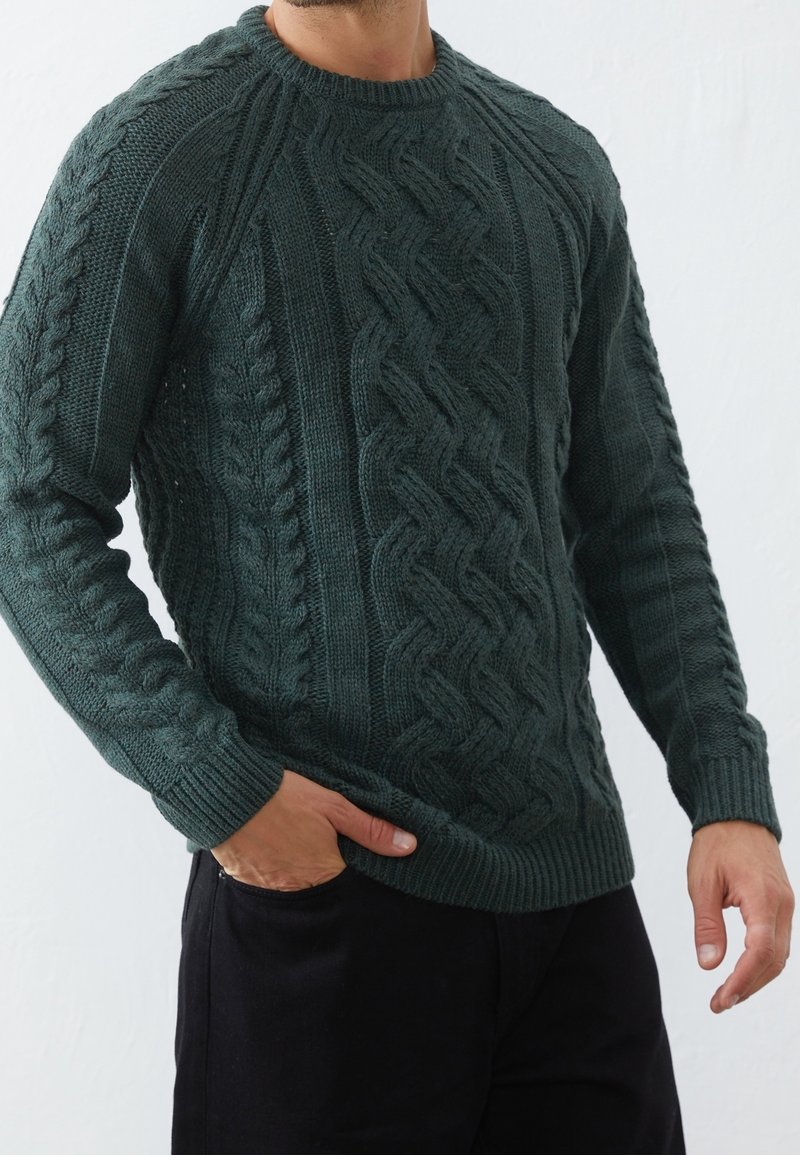 Maglione lavorato a maglia a trecce di un verde scuro con scollo rotondo e polsini a coste. Presenta motivi testurizzati lungo maniche e corpo, realizzato in un filato spesso.