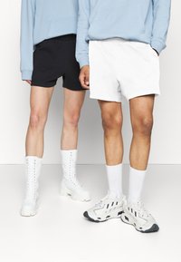 Svarte og hvite shortser i myk stoff, parret med hvite knelange støvler og grå sneakers, stående mot en hvit bakgrunn.