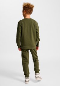 Grünes Sweatshirt- und Hosenset aus weichem Material, mit gerippten Bündchen und Saum, kombiniert mit hellfarbenen Sportschuhen.