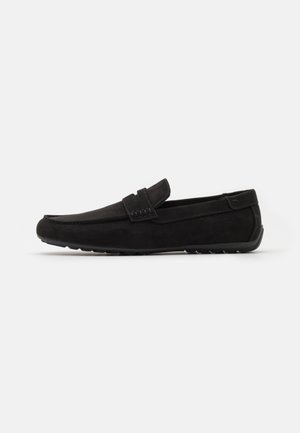 Mocassins de camurça pretos com bico arredondado, detalhes cosidos e um design minimalista. Sola de borracha com um padrão texturizado para aderência.